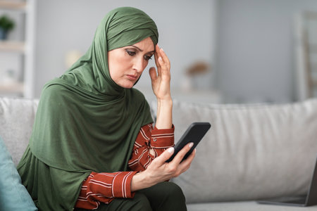 Frustrated Muslim Lady Holding Cellphone Reading Bad News At Home
