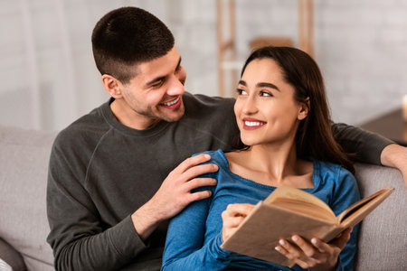 Couple sitting on couch reading book togetherの写真素材