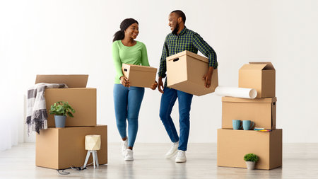 Home Relocation Concept. Joyful African American Spouses Walking With Cardboard Boxes
