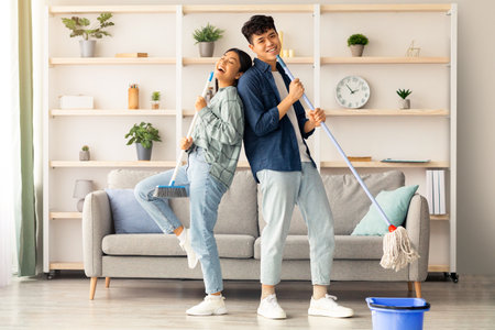 Happy asian couple singing songs while cleaning apartment, copy spaceの写真素材