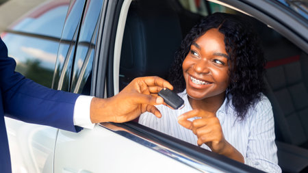 Black Woman Sitting In Car And Taking Key From Salesman In Showroomの写真素材
