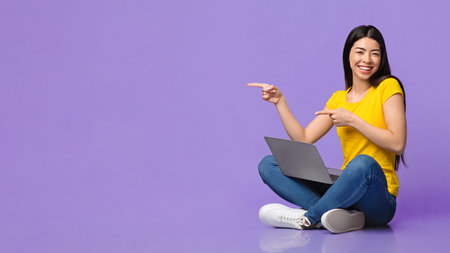 Special Offer. Cheerful asian girl sitting with laptop, pointing at copy spaceの写真素材