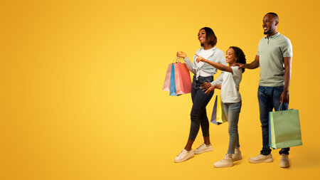 Family shopping. Pretty girl pointing finger at free space, showing something to parents, yellow background, panoramaの写真素材