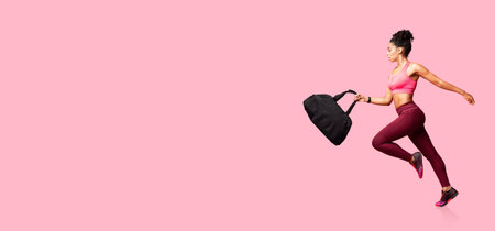 Athletic woman running with a gym bag on a pink background during a workoutの写真素材