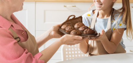 Unrecognizable mature lady and her grandchild with tray of freshly baked muffins in kitchen, closeupの写真素材
