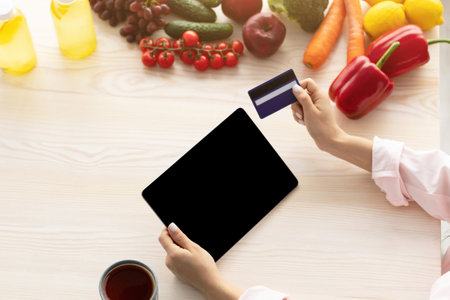 Woman using laptop with in kitchen, holding debit credit cardの写真素材