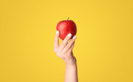 Female hand holding ripe red apple on pink background, close up. Panoramaの写真素材