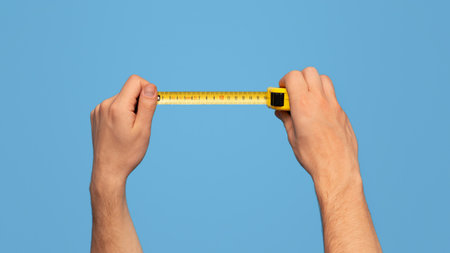 Handyman holding tape measure on blue background, closeup viewの写真素材