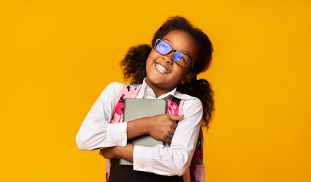 Happy African American Schoolgirl Hugging Book Over Yellow Backgroundの写真素材