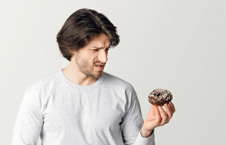 Man holds sweet donut in his hands and looks at it with pain, clutching his hands to stomachの写真素材