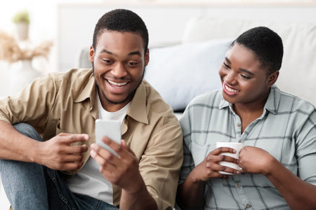 Black Tourists Couple Using Smartphone Browsing Internet Near Suitcase Indoor