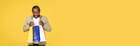 Glad shocked middle aged black man shopaholic in casual looking in package with purchases, enjoy fashionの写真素材