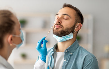 Nasal coronavirus PCR test. Doctor using swab stick to take covid virus specimen from potentially infected young guyの写真素材