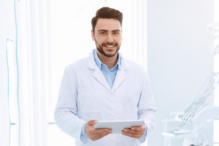 Cheerful bearded man dentist with digital tablet standing by patientの写真素材