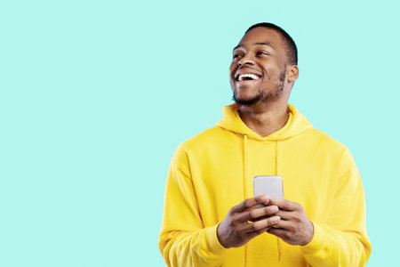 Joyful African Man Using Cellphone Texting Looking Aside, Blue Backgroundの写真素材