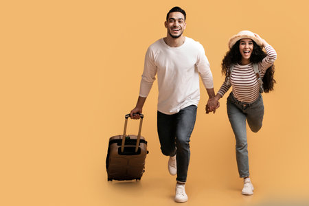 Ready For Vacation. Excited Arab Couple Running With Luggage Over Yellow Backgroundの写真素材