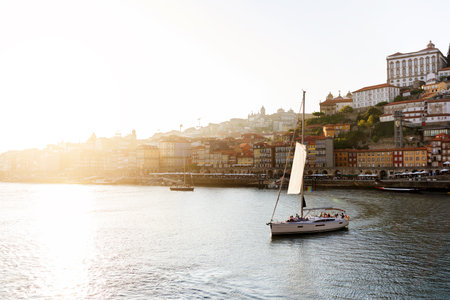 Sailboat gliding on the Douro River with Portos colorful skyline at sunsetの写真素材