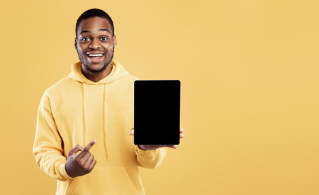 Black Man Pointing At Digital Tablet Empty Screen, Yellow Backgroundの写真素材