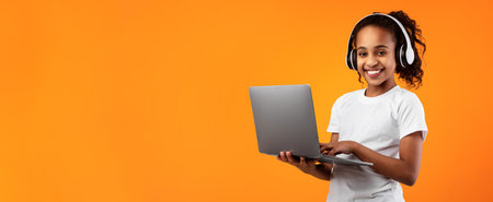Black girl in headphones standing with laptop at studioの写真素材