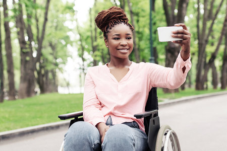 Full length photo of a person in wheelchair taking selfie on cellphone at parkの写真素材