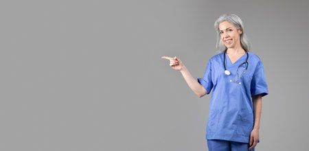 Middle aged lady doctor in scrubs pointing to the side with a smileの写真素材