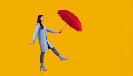 Portrait of excited young woman holding umbrella at studioの写真素材