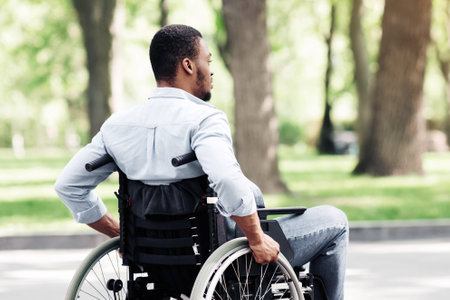 Thoughtful young black guy in wheelchair having walk at urban park, copy spaceの写真素材