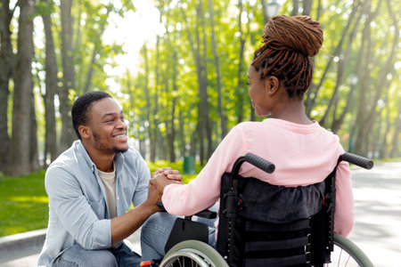 Tender black guy holding his disabled girlfriends hand, expressing love and affection at city parkの写真素材