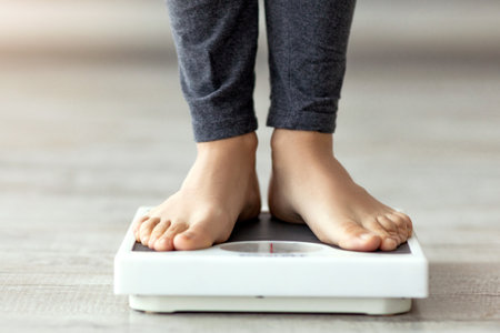 Unrecognizable Indian woman standing on scales, checking her weight indoors, closeup of feetの写真素材