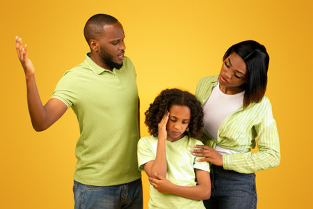 Young black father shouting at daughter and mother comforting upset little girl, hugging and consoling herの写真素材