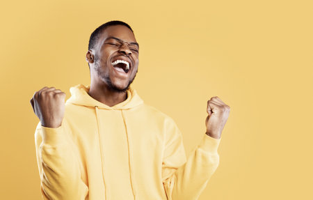 Emotional Black Man Shouting Shaking Fists Celebrating Success, Yellow Backgroundの写真素材