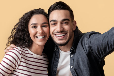 Romantic Cheerful Arab Couple Taking Selfie Together Over Yellow Background,