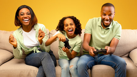 Domestic entertainment. Emotional black dad and daughter playing video games, sitting on sofa over...