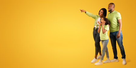 Wow offer. Full body length portrait of excited black family looking and pointing at copy space on yellow backgroundの写真素材