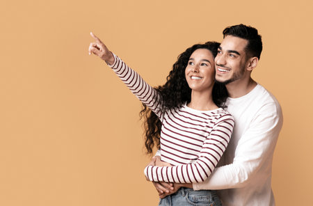 Cheerful Young Arab Couple Pointing With Finger Aside At Copy Spaceの写真素材