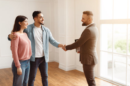 Millennial Couple Buying New Apartment, Shaking Hands With Realtorの写真素材