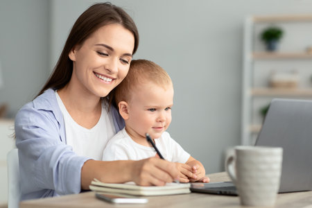 Online Education. Young Woman Holding Baby And Study With Laptop At Homeの写真素材