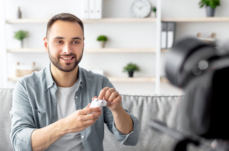 Popular male blogger shooting video review of new earhpones, using professional camera at home