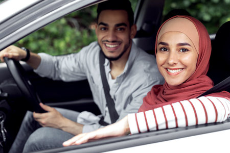Smiling millennial man at steering wheel and woman in hijab ride in car, enjoy travel together outdoorの写真素材