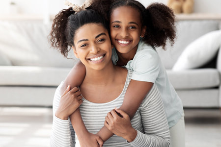 Sporty black mother and daughter sitting on fitness mat, embracingの写真素材