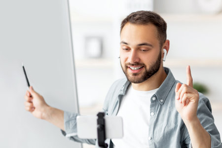 Happy male teacher giving online private lesson from home, pointing at empty blackboard with empty spaceの写真素材