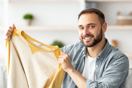 Satisfied male client taking out new sweater from cardboard box, happy with delivery service at homeの写真素材
