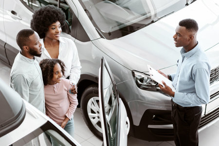 Car sales business concept. Above view of manager talking to Afro family with cute kid, selling auto at dealership shopの写真素材