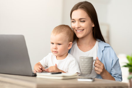 Technology And Childcare. Mother Drinking Tea While Baby Watching Cartoons On Laptopの写真素材