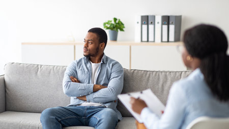 Young psychologist working with emotionally detached black male patient at clinic, trying to help him with depressionの写真素材