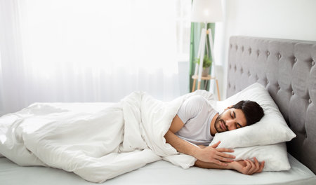 Bedtime. Tired millennial arab man asleep, resting peacefully in white comfortable bed in bedroom,...
