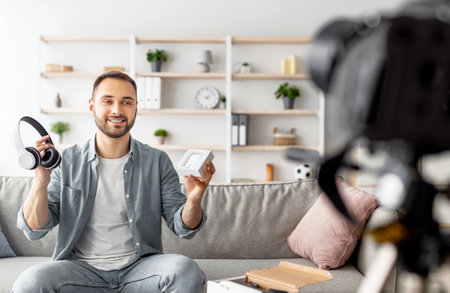 Young male influencer recording video review, comparing new wireless headphones and earphones models at homeの写真素材