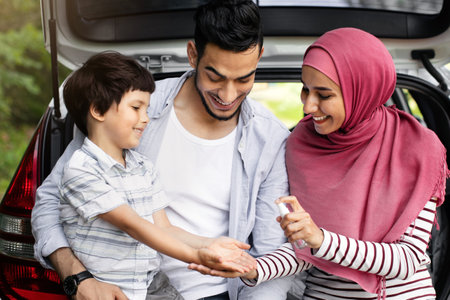 Travels During Pandemic. Muslim Family With Son Applying Disinfectant Spray On Handsの写真素材