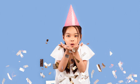 Kid Girl Blowing Silver Confetti Celebrating Birthday Over Purple Backgroundの写真素材
