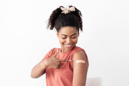 Glad black woman pointing at medical band on shoulderの写真素材